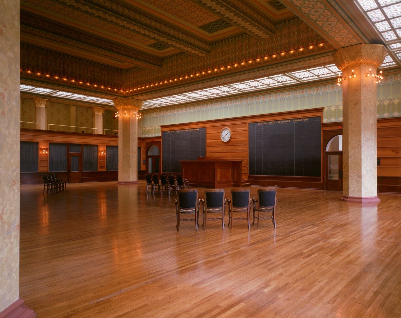 The trading room of the Chicago Stock Exchange: a tall hall with stencilled walls, quotation boards and a polished wooden floor